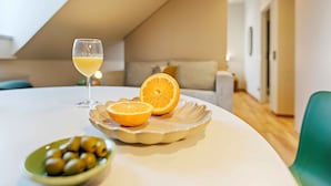 A dining table with a glass of white wine, a plate with an orange slice and olives, and a bowl of olives.
