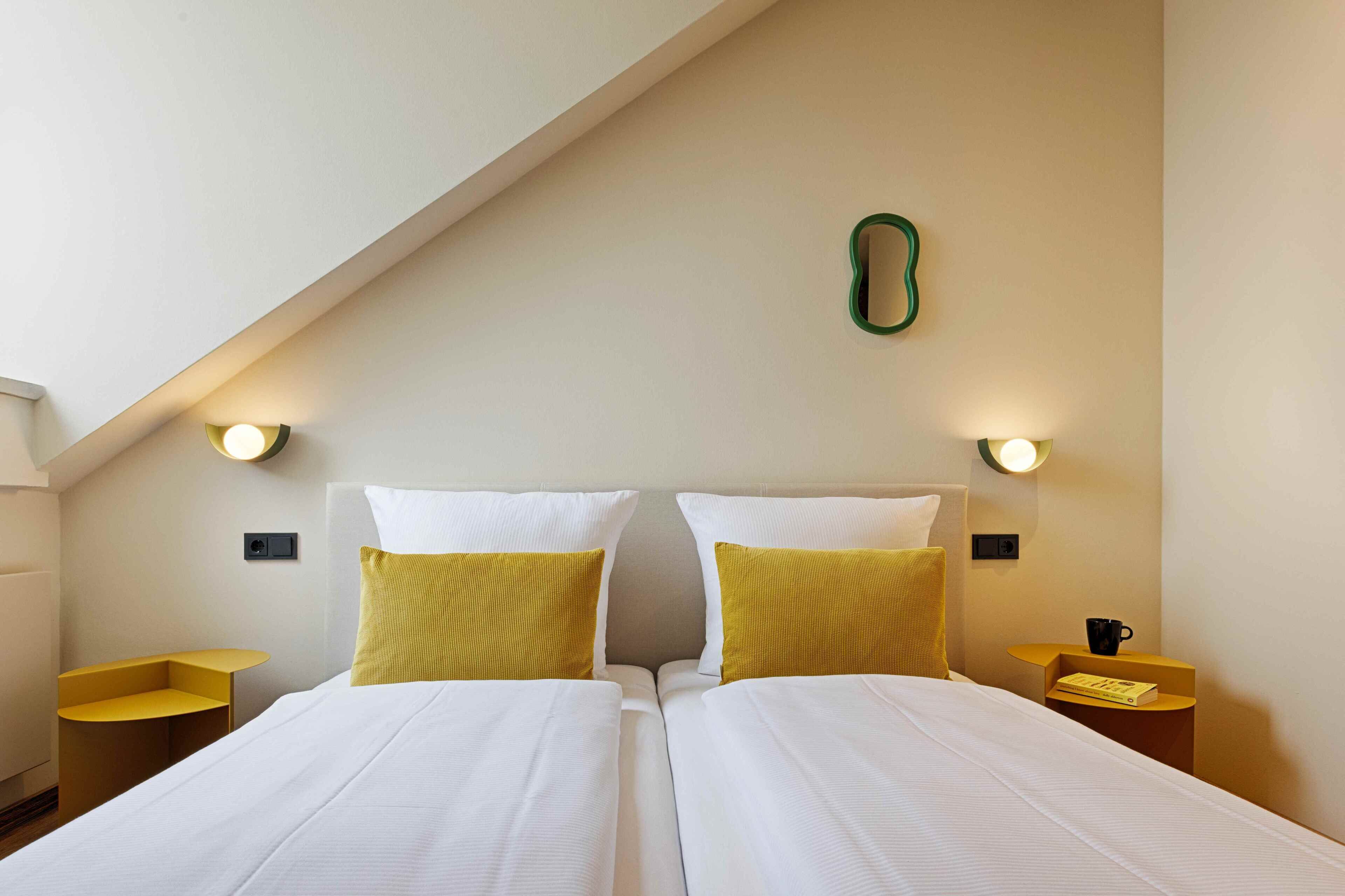 A hotel room with two beds, a sloped ceiling, and wall-mounted lights.
