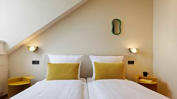 A hotel room with two beds, a sloped ceiling, and wall-mounted lights.