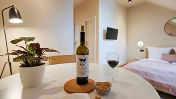 A room with a bed, a table with a wine bottle, a glass of wine, a potted plant, and a bowl of nuts.