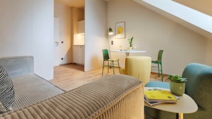 A modern living room with a sofa, a small round table with a plant, and a dining area with chairs and a table.