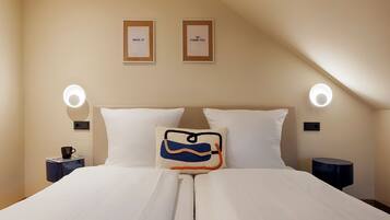 A neatly made bed with white linens, two pillows, a decorative pillow with a blue and orange design, and two wall-mounted lamps.