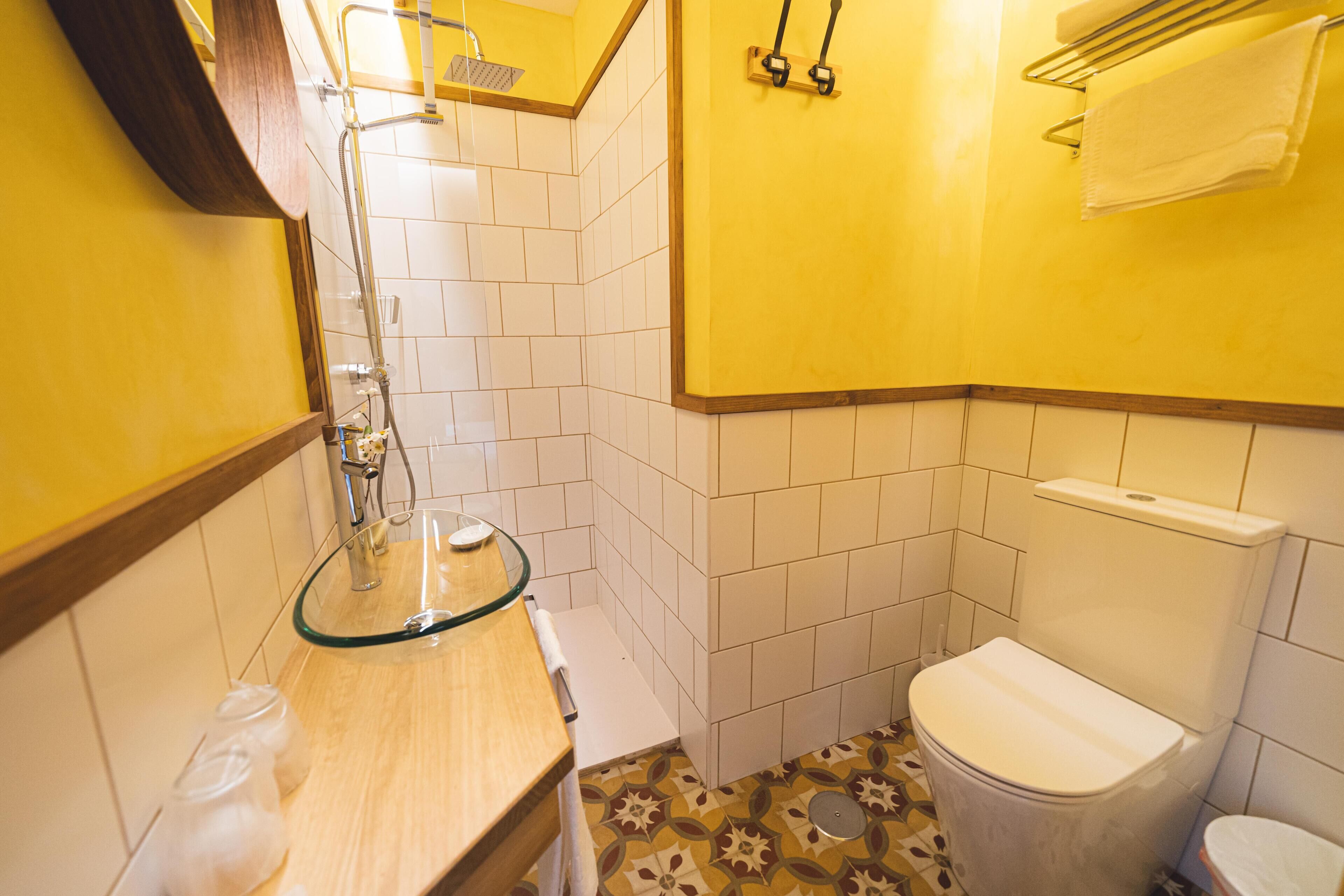 A small bathroom with a glass sink, white tiles, and a toilet.