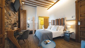Un dormitorio con cama, mesita de noche, lámpara y televisor montado en la pared.