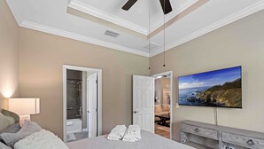 Ein Schlafzimmer mit Bett, Fernseher, Kommode und angrenzendem Badezimmer.