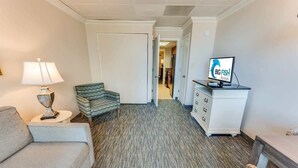 Une chambre d’hôtel équipée d’un canapé, d’un fauteuil, d’une lampe, d’une télévision et d’une commode.