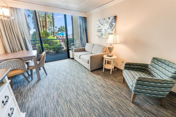 A hotel room with a balcony, a sofa, a chair, a small table, and a lamp. - Heated pools and direct oceanfront at Coral Beach (Myrtle Beach)
