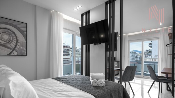 Moderni hotellihuone, jossa on suuri sänky, taulutelevisio, parveke, jolta on näkymä kaupunkiin, sekä ruokailutila.