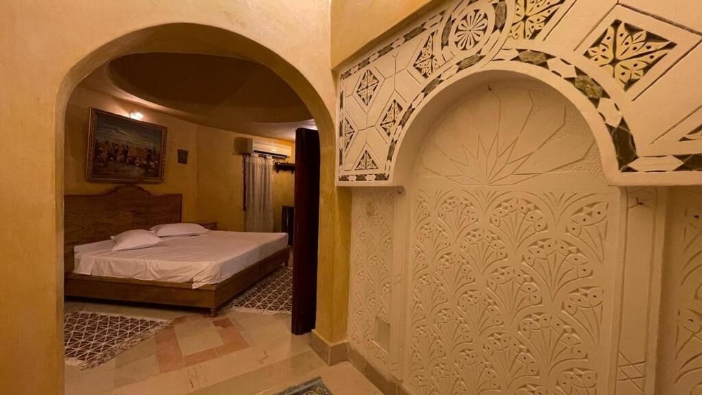 A hotel room with a bed, a patterned wall, and an arched doorway.