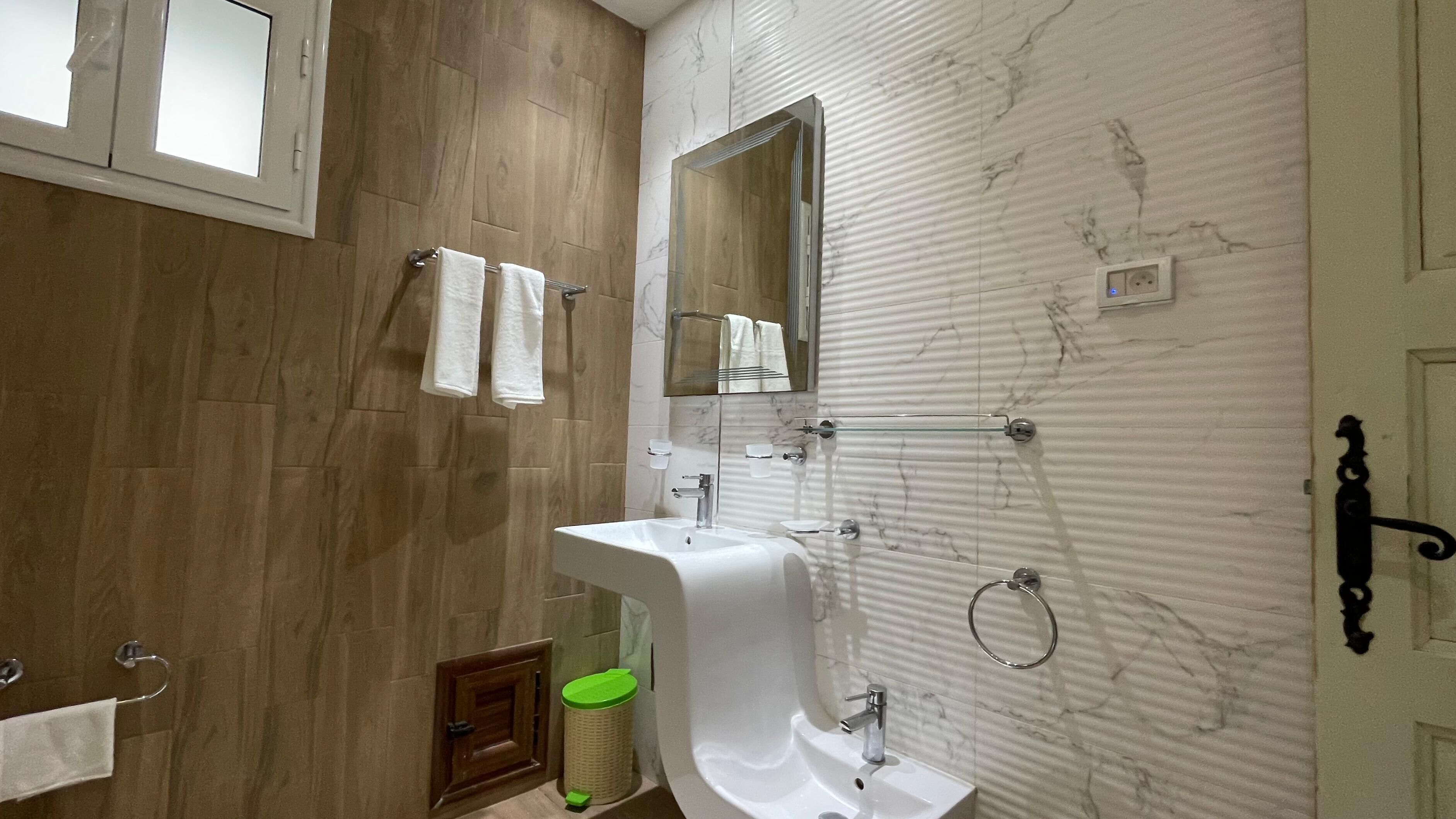 A modern bathroom with a wooden floor, a white sink with a mirror above it, and a towel rack.