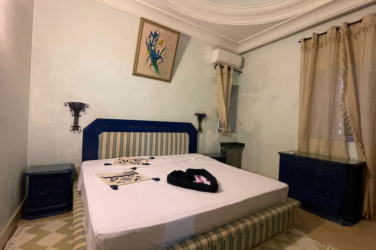 Quarto com cama, mesas de cabeceira, cômoda, espelho e um quadro na parede.