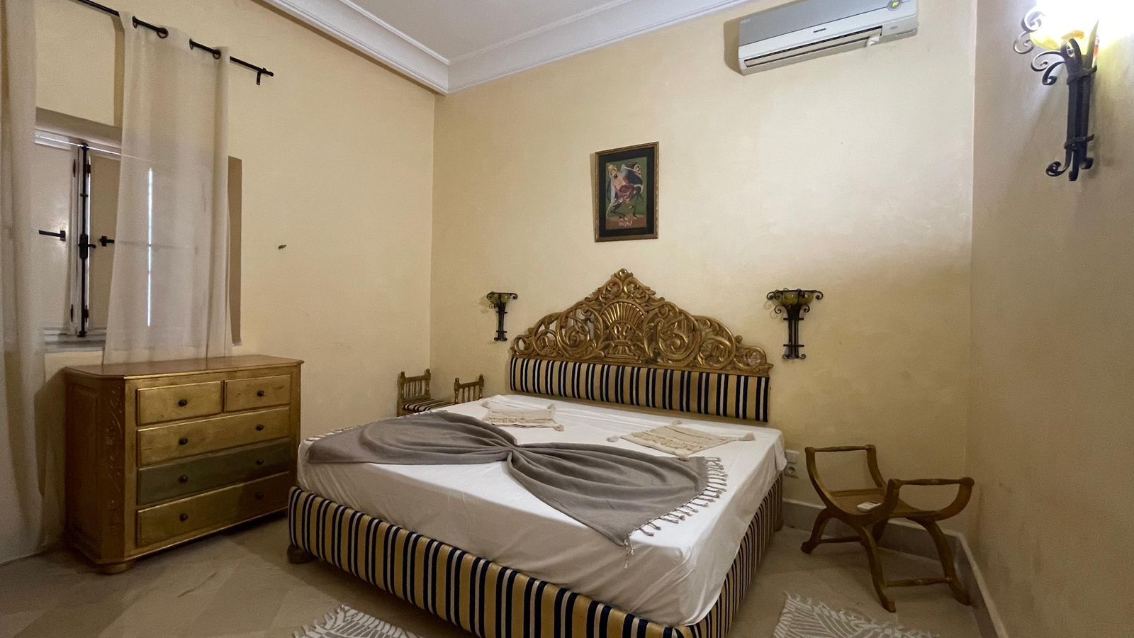 A bedroom with a bed, dresser, chairs, and a picture on the wall.