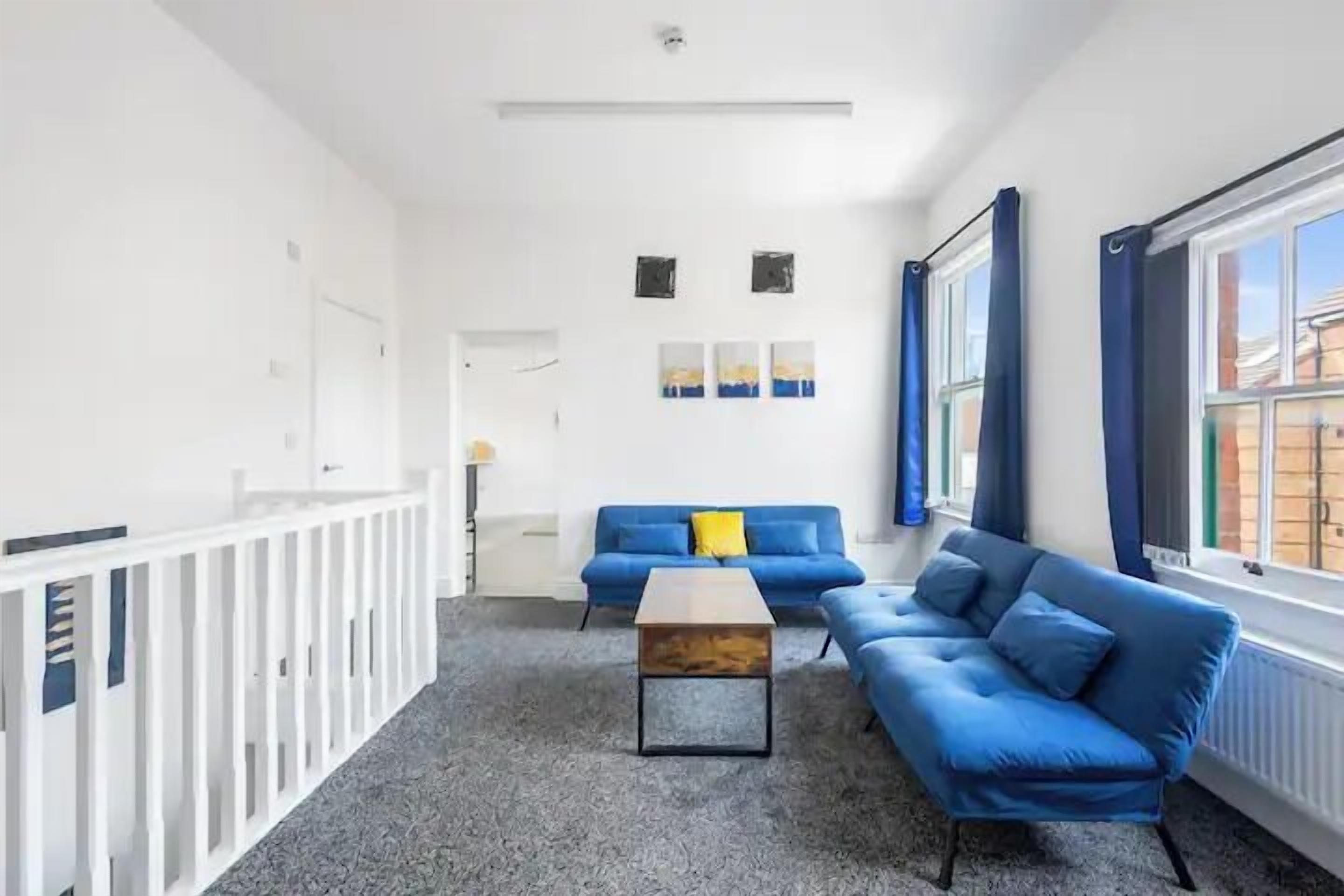 A modern living room with a blue sofa, a wooden coffee table, and a white railing.
