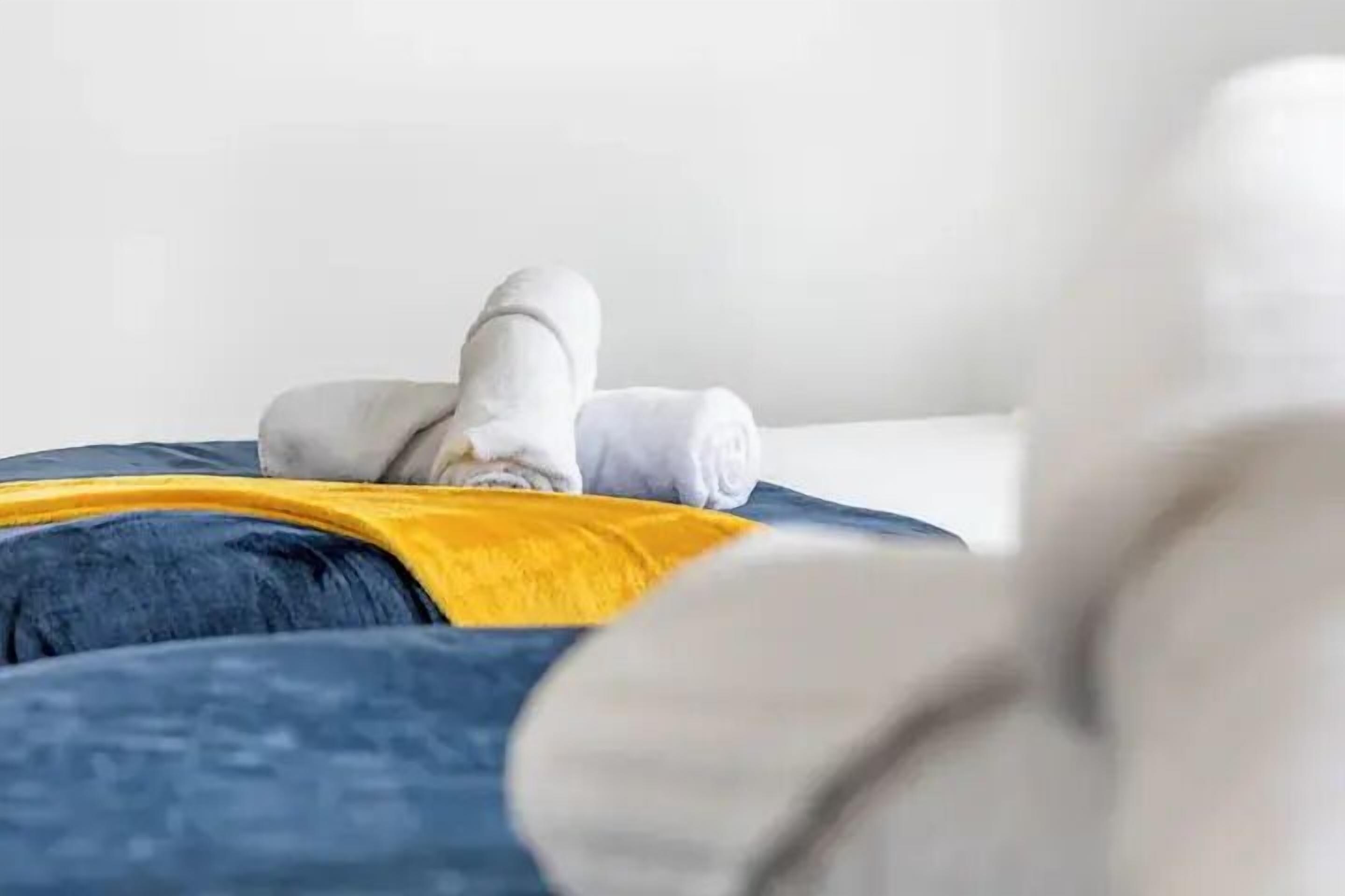 Una cama con un edredón amarillo y una toalla blanca enrollada.