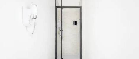 A modern bathroom with a glass shower enclosure, a white wall-mounted towel dispenser, and a visible ventilation vent.