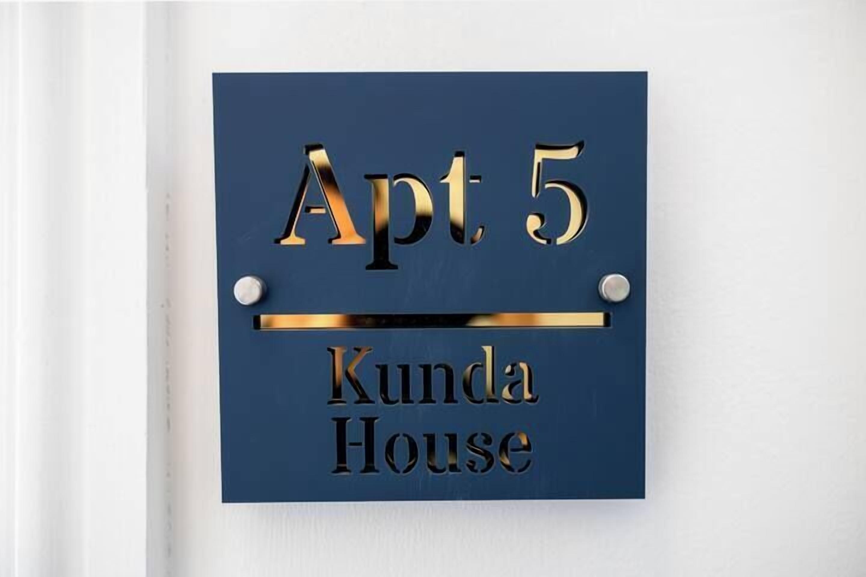 A sign with "Apt. 5 Kunda House" written in gold on a blue background.