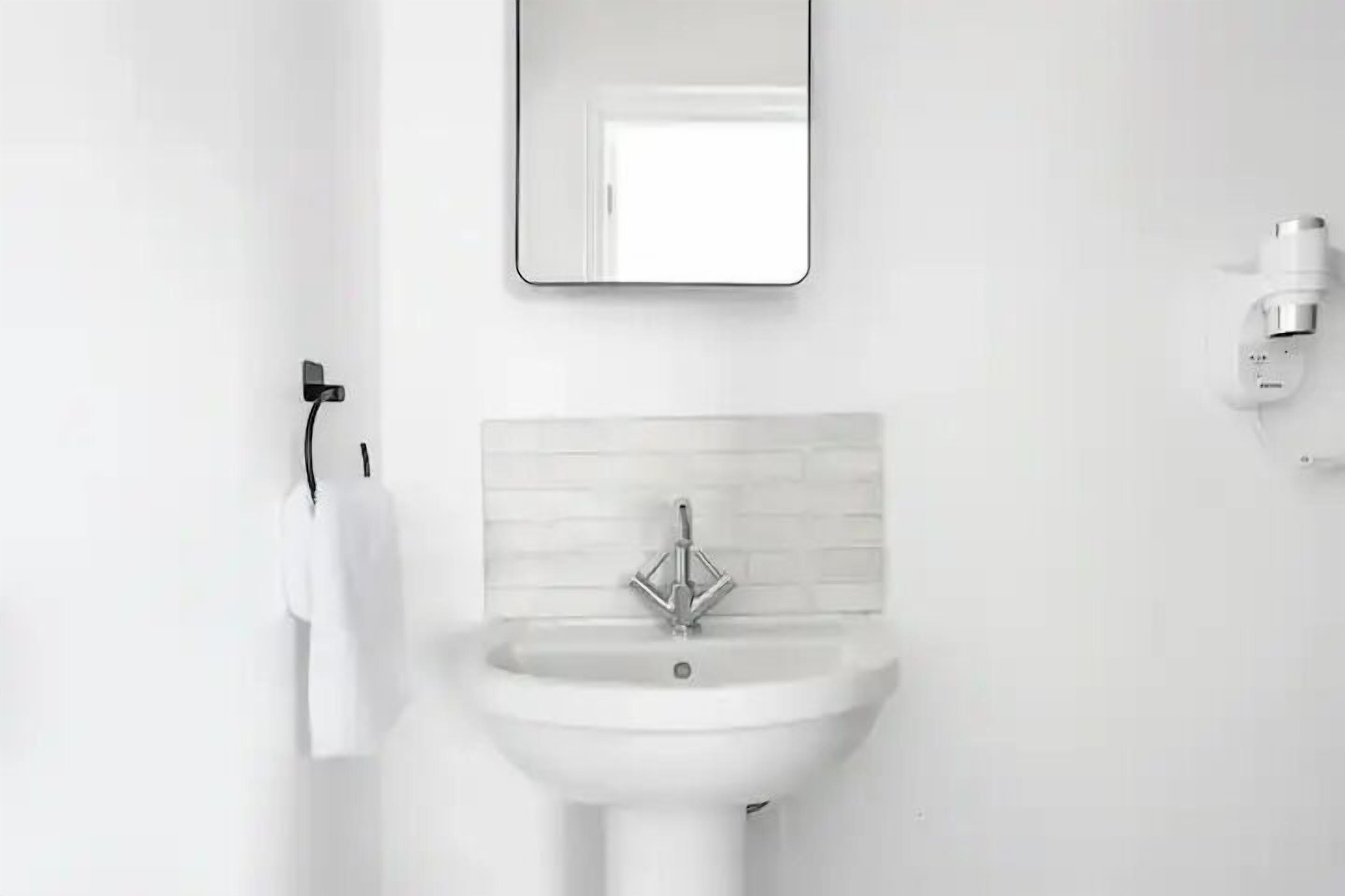 Un baño con un lavabo blanco, un espejo y un perchero para toallas.