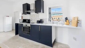 Une cuisine moderne avec des meubles de couleur sombre, un plan de travail blanc et une fenêtre donnant sur l’extérieur.