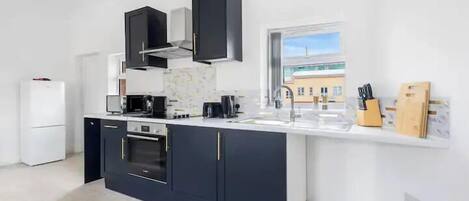 A modern kitchen with dark cabinetry, a white countertop, and a window providing a view of the outside.