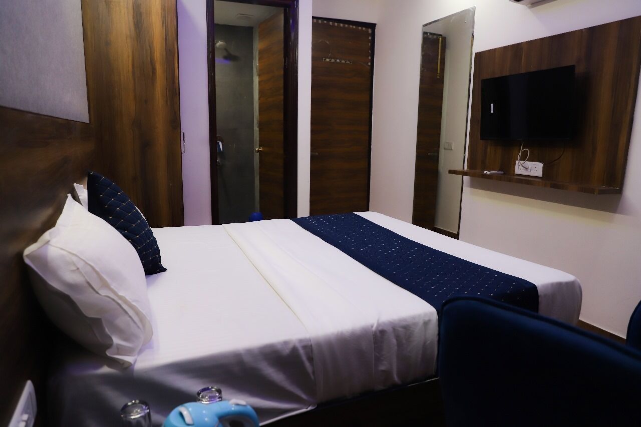 A hotel room with a bed, a TV mounted on the wall, and a mirror above the bed.