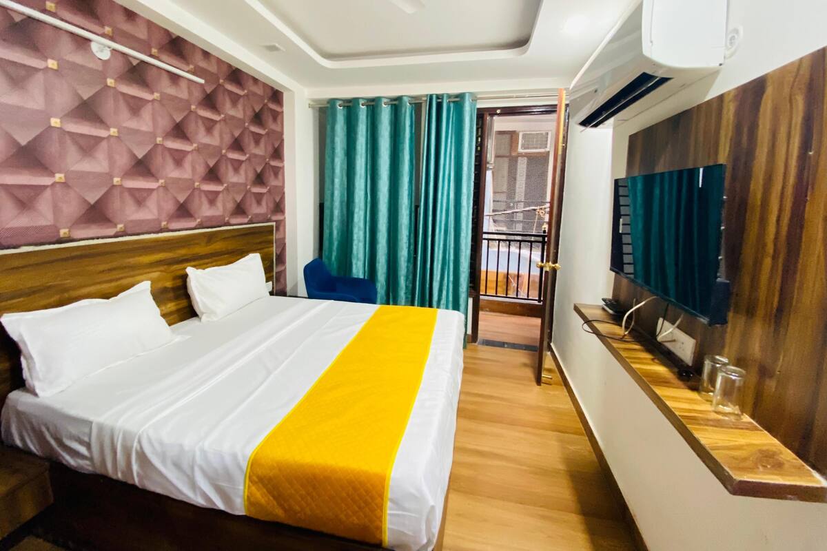 A hotel room with a bed, a TV, a wooden desk, and a balcony with a railing.