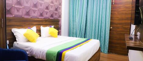 A hotel room with a bed, a blue chair, a wooden headboard, a TV, and a curtain.