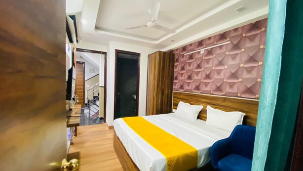 A hotel room with a bed, a desk, a chair, a ceiling fan, and a staircase. - Hotel Surya International (New Delhi)