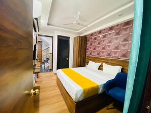 A hotel room with a bed, a desk, a chair, a ceiling fan, and a staircase. - Hotel Surya International (New Delhi)
