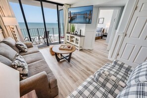 A living room with a sofa, a coffee table, and a TV. There is a balcony with a view of the sea. - Direct Ocean View - Exclusive Sand Beach Club 2BR (Myrtle Beach)
