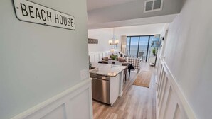 A modern kitchen with a central island, a dining area with a view, and a sign reading "BEACH HOUSE". - Direct Ocean View - Exclusive Sand Beach Club 2BR (Myrtle Beach)