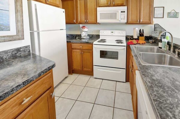 A kitchen with wooden cabinets, a white refrigerator, a microwave, a stove, and a sink.