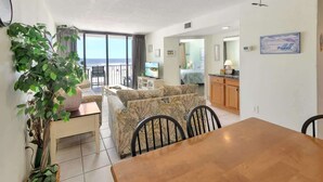 A living room with a sofa, dining table, and chairs. There is a plant and a TV in the room. - New, Low Floor, Direct Ocean View Sands Beach Club (Myrtle Beach)
