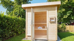 A wooden outdoor sauna with a door open, revealing towels and a bucket inside. - "Experience luxury and relaxation at the Buhne 44 vacation home on Sylt!" (List auf Sylt)