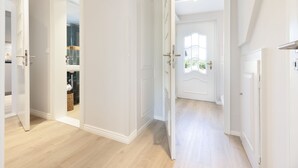 A hallway with white walls and wooden flooring, leading to a room with a large window and a door with a decorative design. - "Experience luxury and relaxation at the Buhne 44 vacation home on Sylt!" (List auf Sylt)