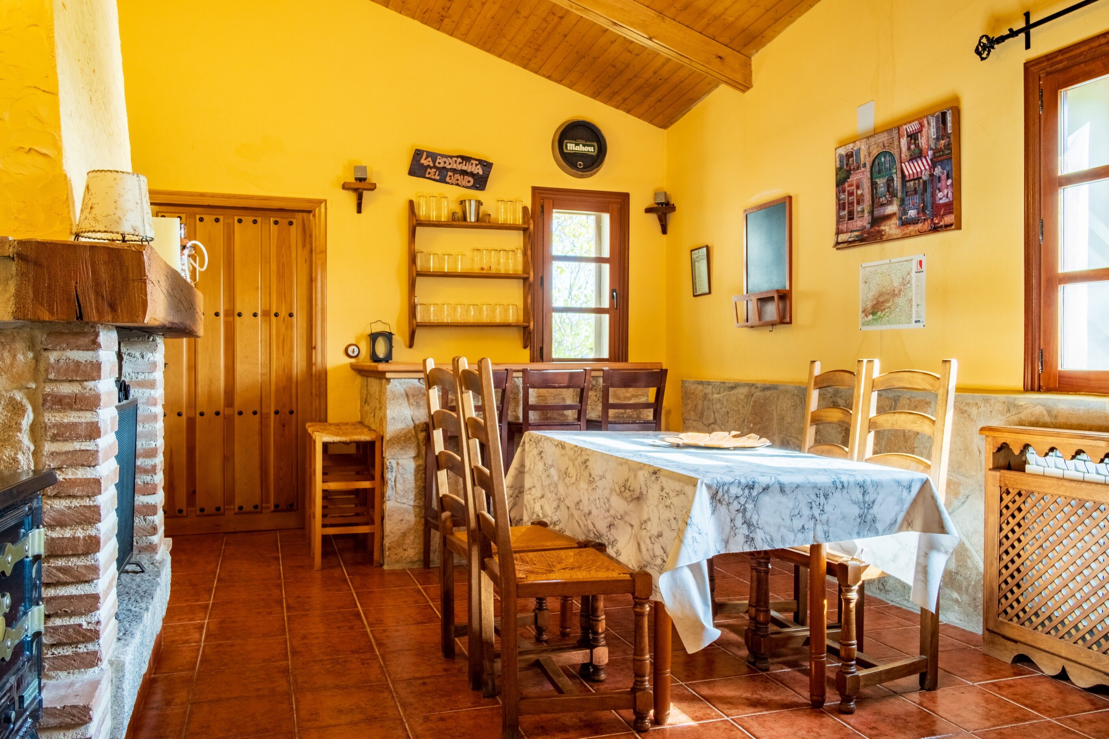 Un comedor con una mesa dispuesta para cuatro personas, sillas de madera, una chimenea de ladrillo y una puerta de madera.