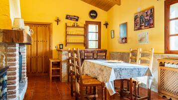 Un comedor con una mesa dispuesta para cuatro personas, sillas de madera, una chimenea de ladrillo y una puerta de madera.