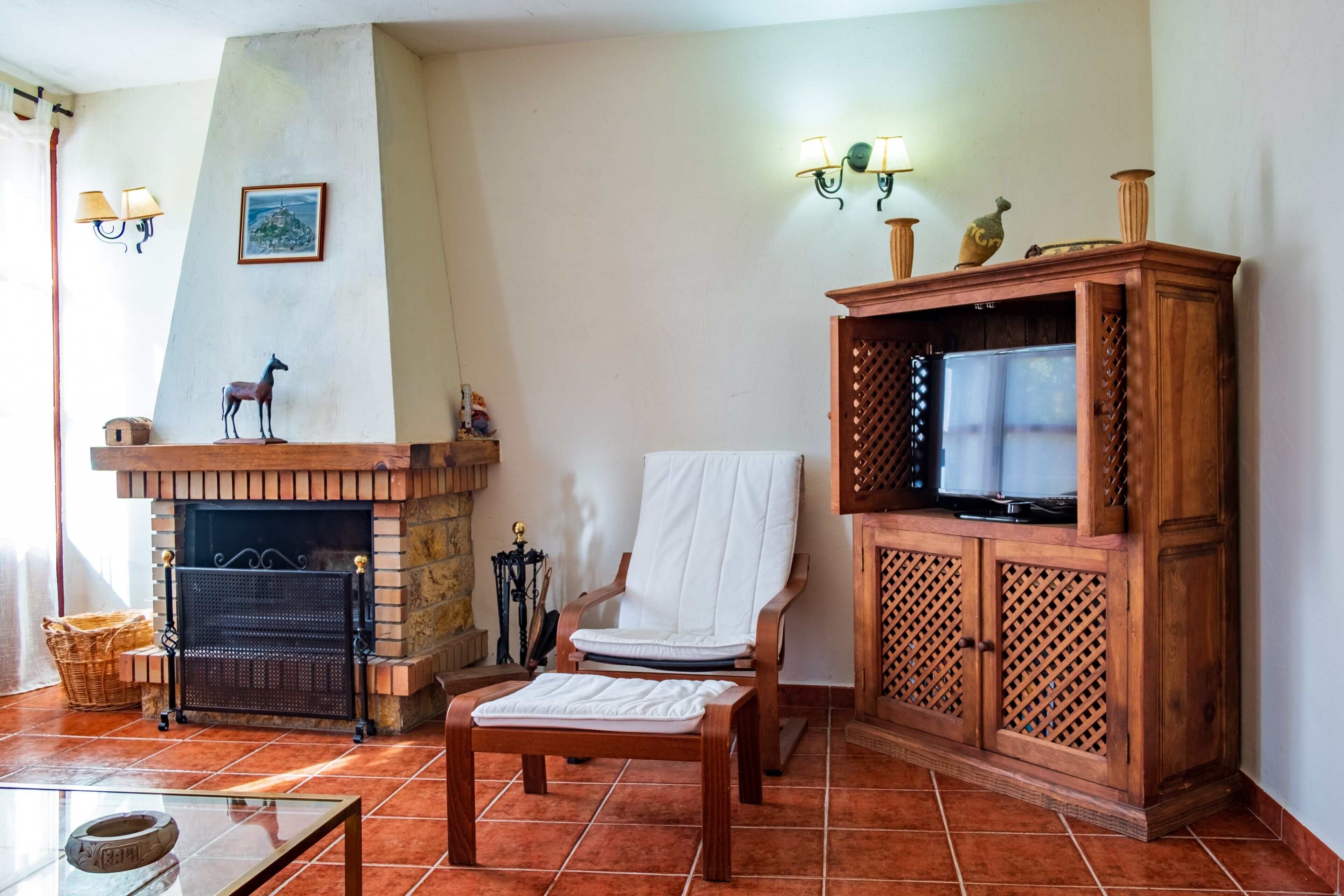 Un salon avec une cheminée, un téléviseur, un fauteuil blanc et un meuble en bois.