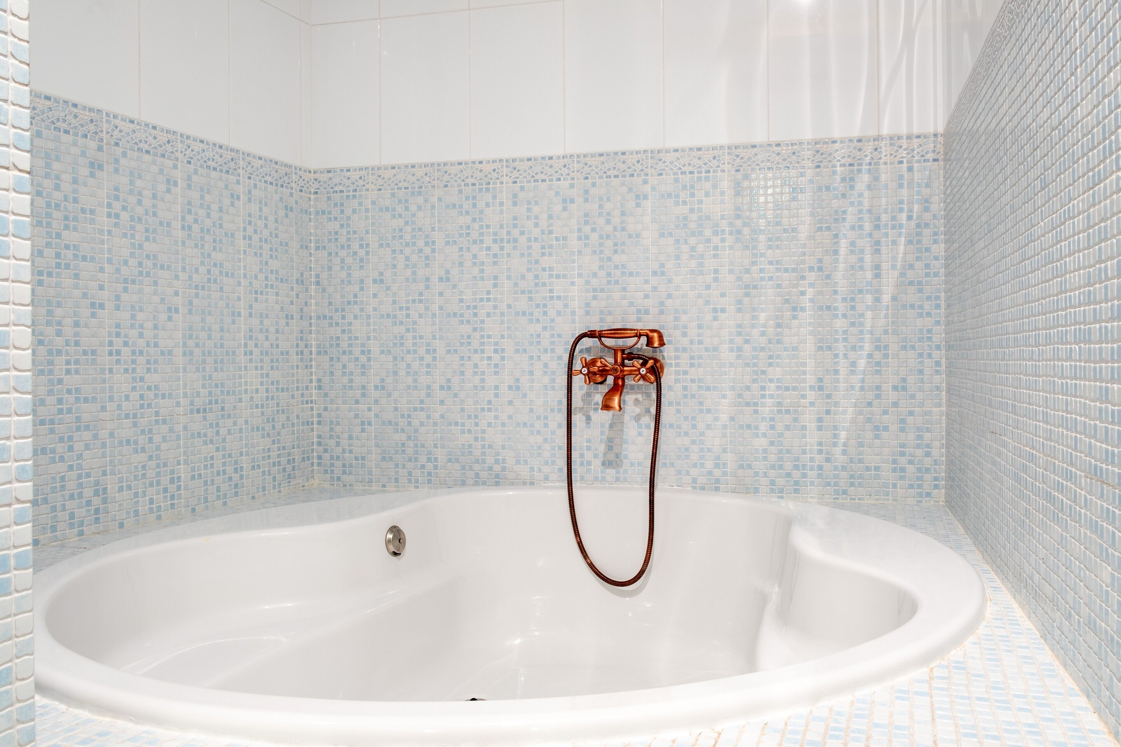 Une salle de bain avec une baignoire blanche, des carreaux de mosaïque bleus et une pomme de douche en cuivre.