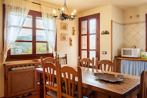 Ein Essbereich mit Holzsesseln und einem Tisch, ein Fenster mit Vorhängen, eine Kristallleuchter und eine Mikrowelle auf einer Arbeitsplatte.