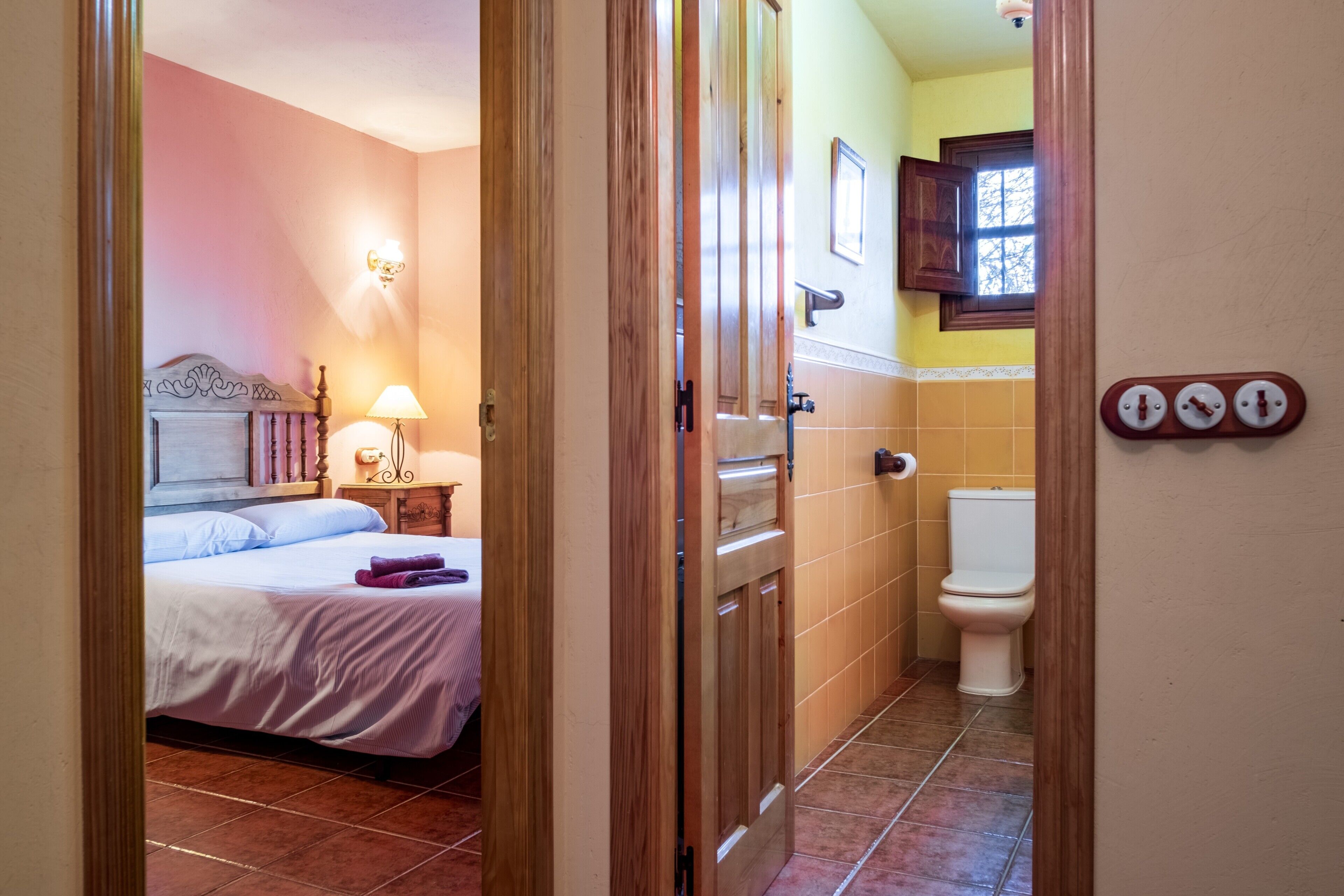 Un dormitorio con cama, lámpara de noche y baño con inodoro y lavamanos.