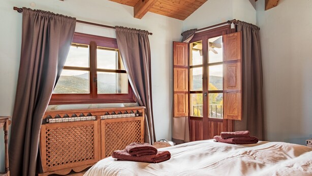 Una habitación con cama, cabecero de madera, ventana con cortinas y vistas al exterior.