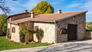 Un edificio de piedra con techo de tejas, puerta de madera y un pequeño pozo para rueda.