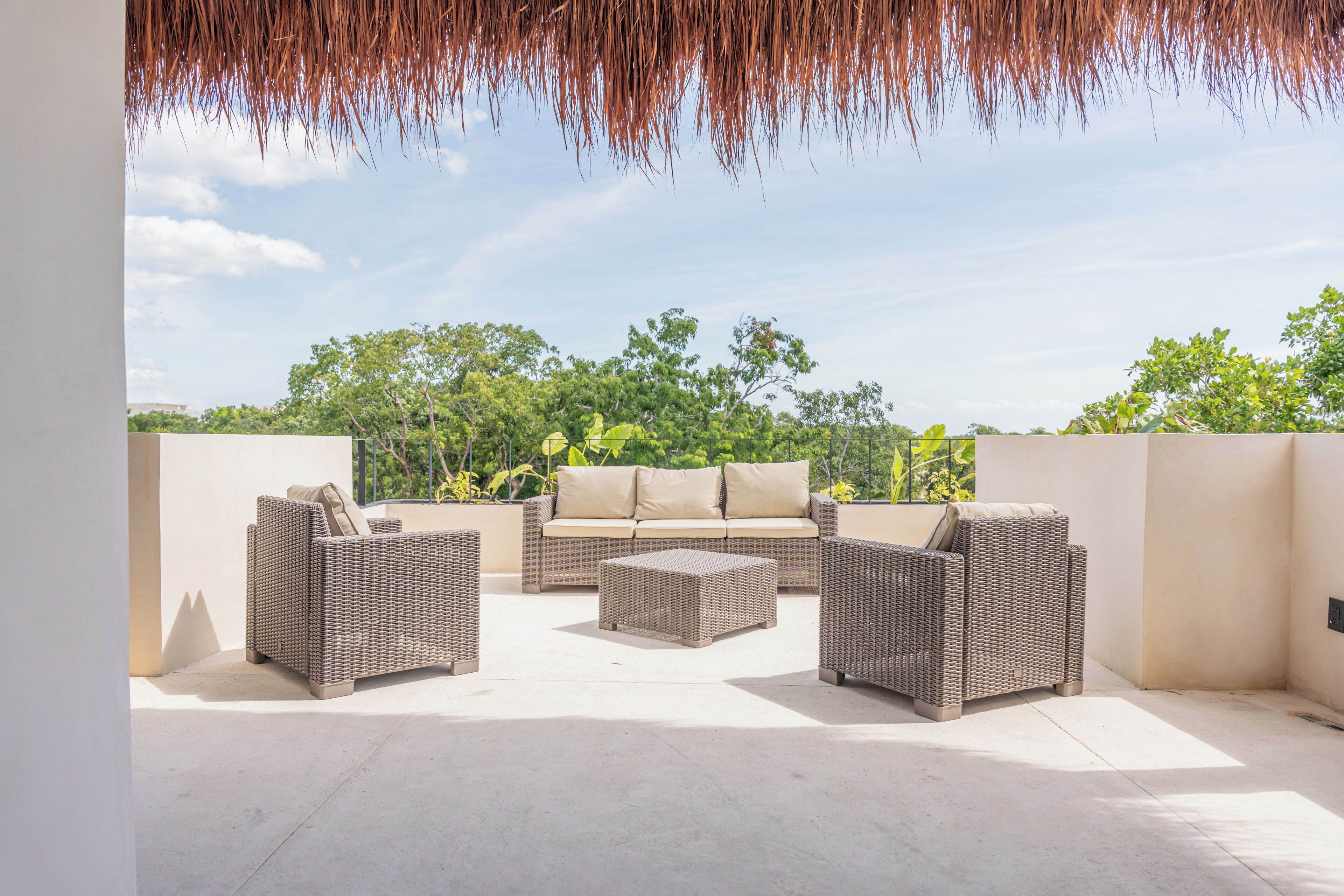 An outdoor patio area with wicker furniture, including a sofa and two armchairs, and a small ottoman.