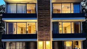 Un bâtiment moderne à plusieurs étages, doté de grandes fenêtres, d’un élément vertical central et d’un toit en chaume.