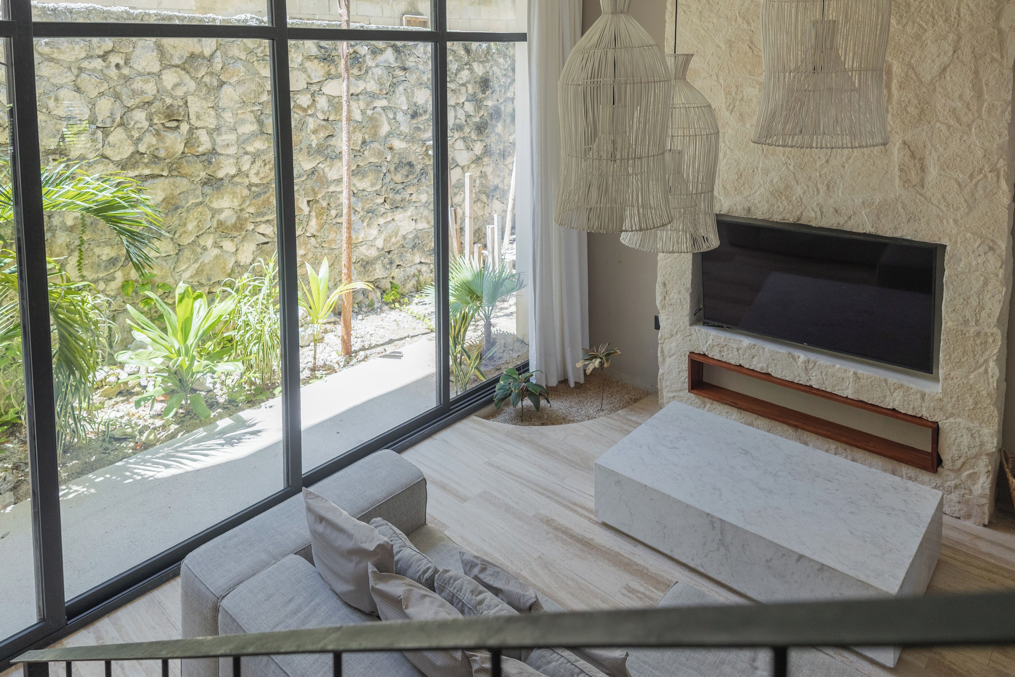 A modern living room with a stone wall, large windows, a flat-screen TV, and a minimalist sofa.