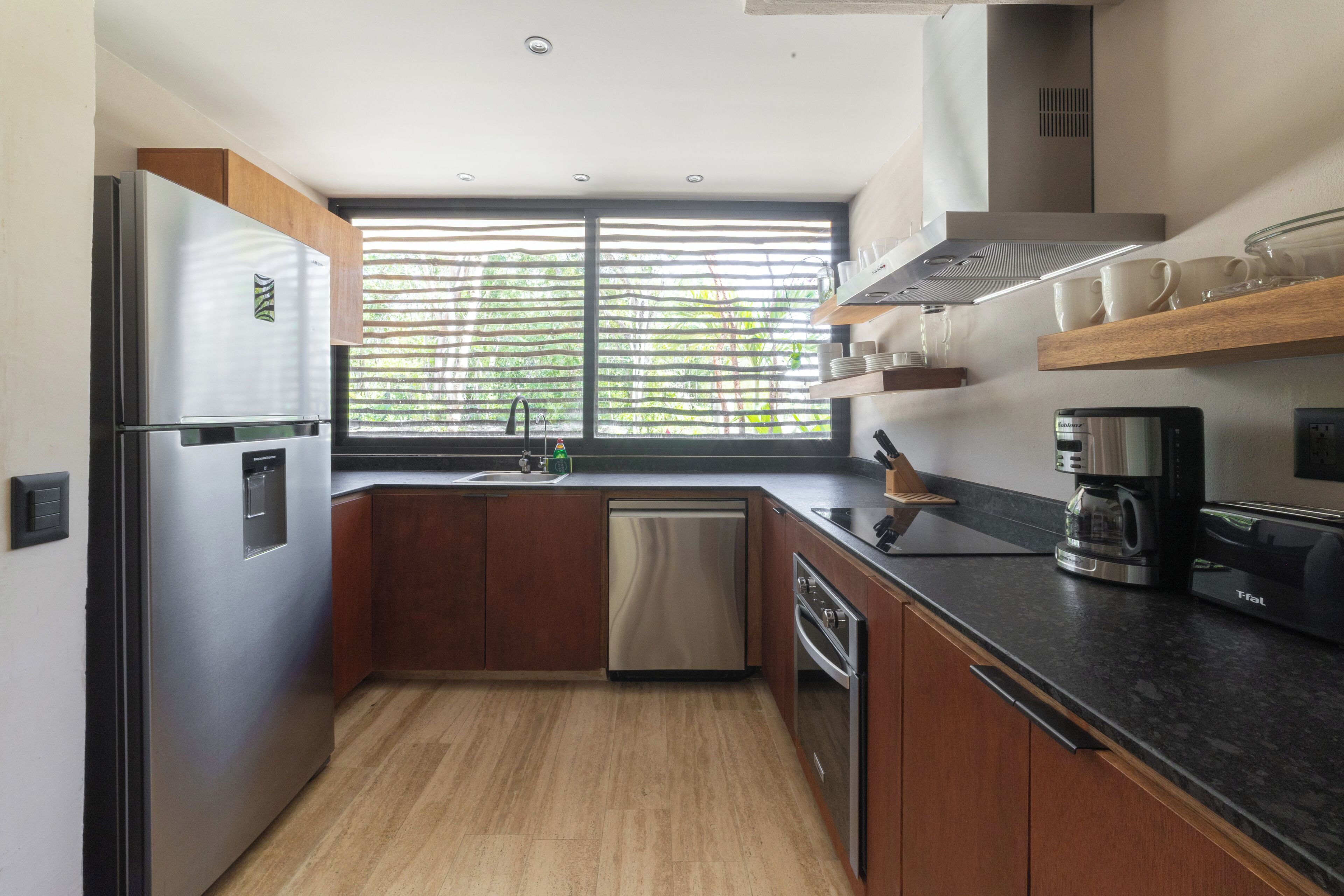 Een moderne keuken met een roestvrijstalen koelkast, houten kastjes, een vaatwasser en een koffiezetapparaat.