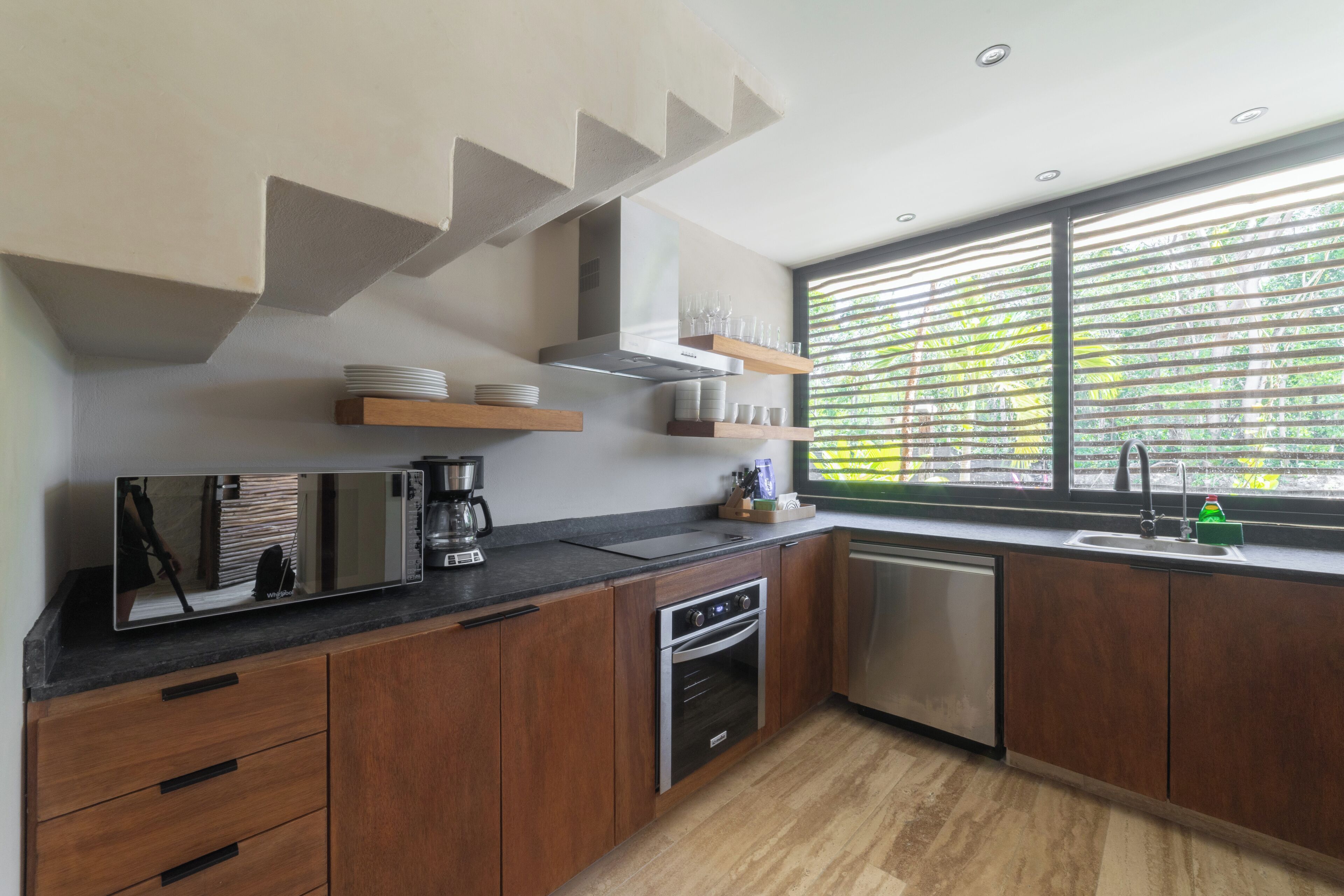 A modern kitchen with wooden cabinets, a built-in oven, a dishwasher, and a large window with blinds.