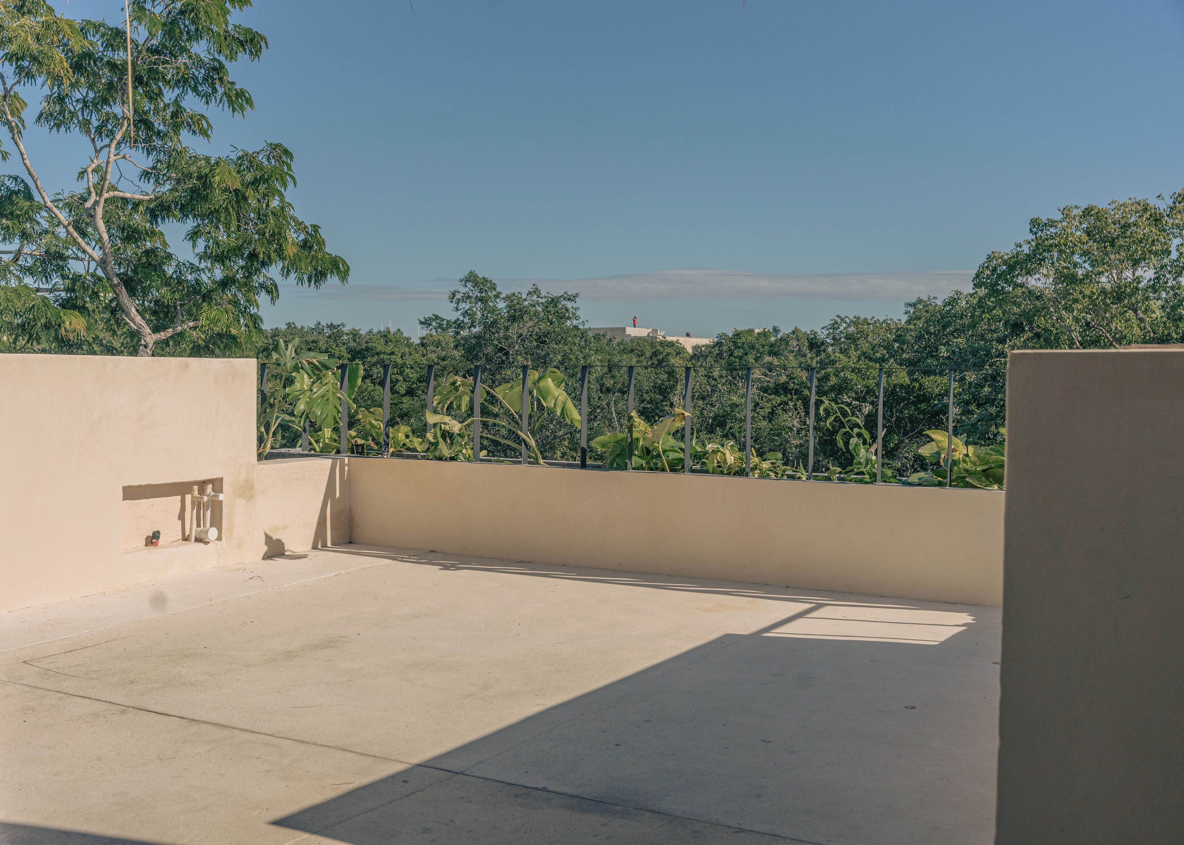 A rooftop terrace with a concrete floor, a beige wall, and a metal railing.