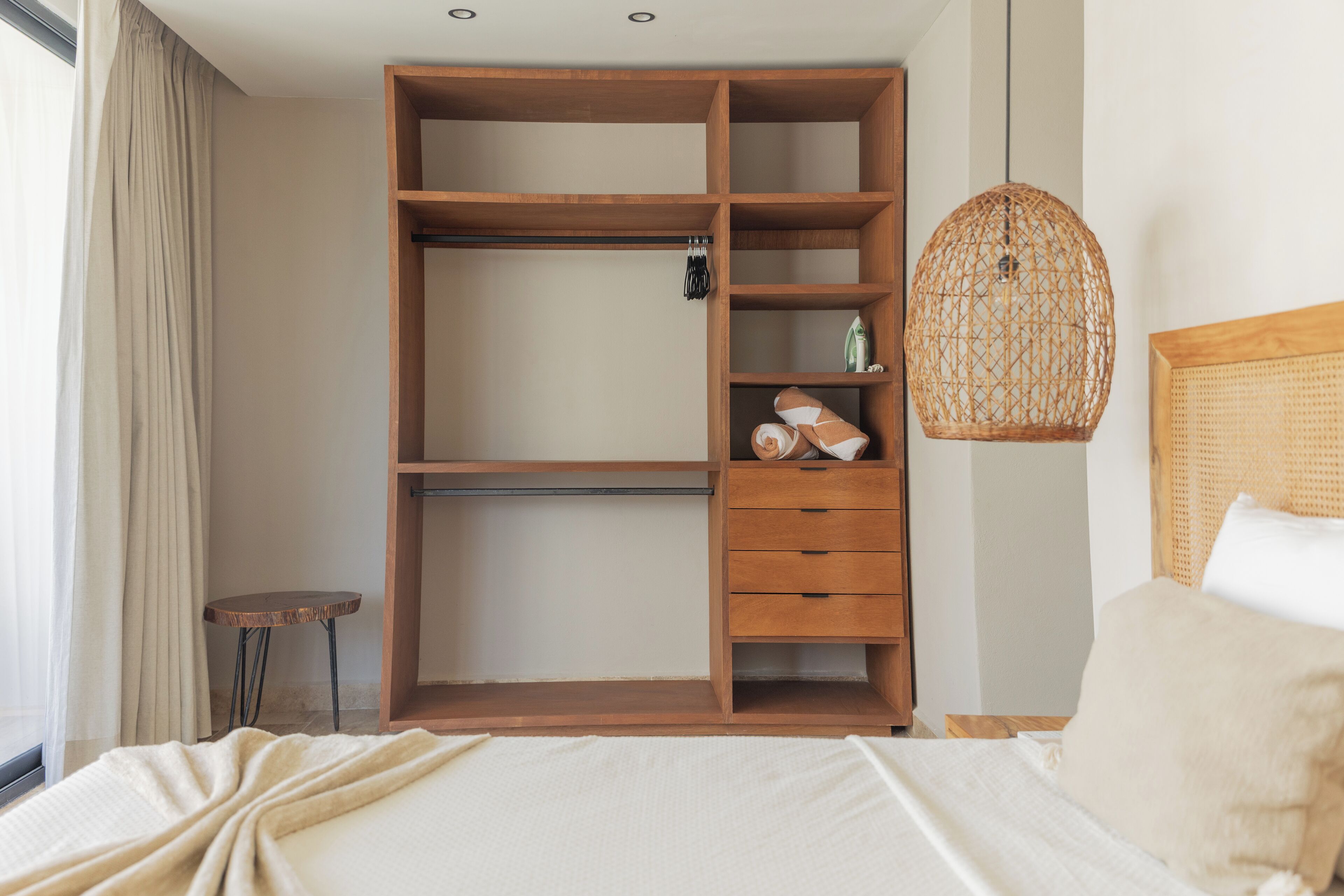 Ein Schlafzimmer mit einem Holzschrank, einem Nachttisch, einer hängenden Korbschaukel-Lampe und einem Bett mit weißer Bettwäsche.