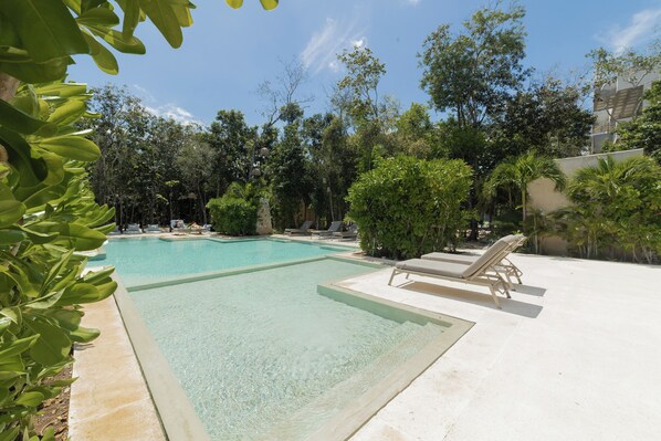 A clear swimming pool with lounge chairs and lush greenery around. - BT Homes - Zama Luxury (Tulum)